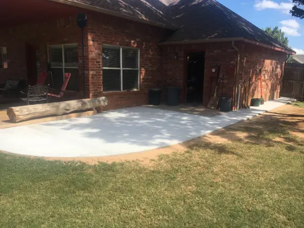 Backyard with concrete patio, red brick house, and green grass.