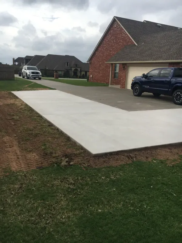 New concrete driveway leading to a brick house with two parked vehicles on a cloudy day.