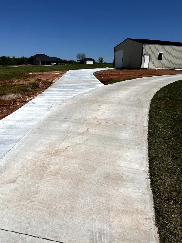 Concrete driveway curves toward a beige building with a white door; blue sky.