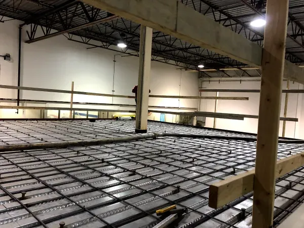 Interior view of a construction site: Metal rebar grid laid for a concrete floor, with support beams and a high ceiling.