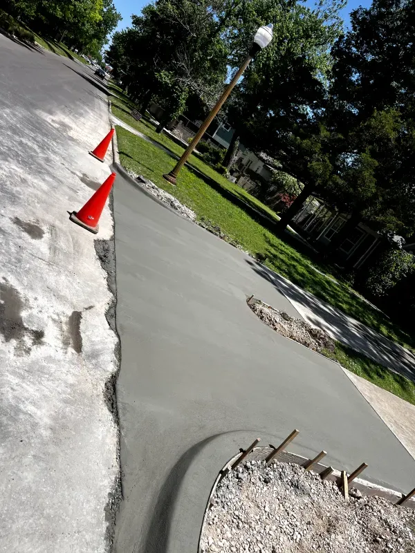 Newly poured concrete walkway next to a road, with safety cones in place.