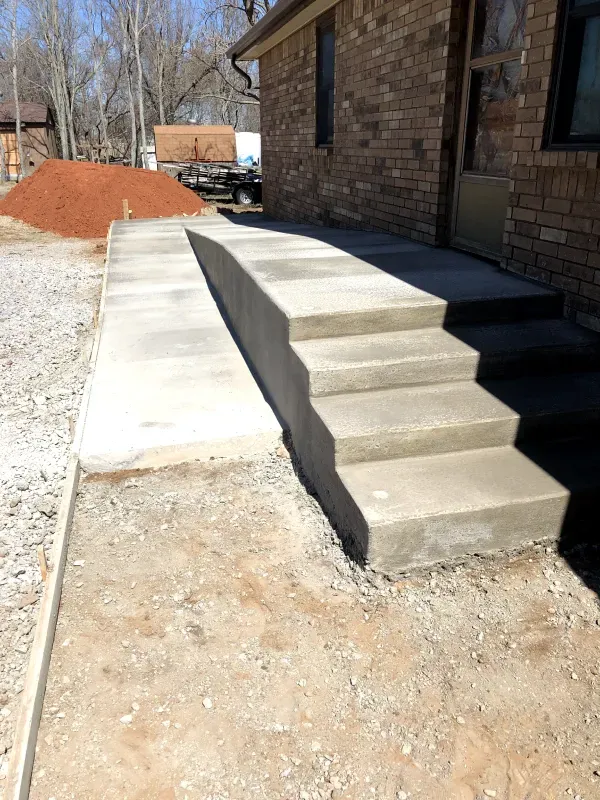 Concrete ramp and steps leading to a brick building entrance. Gravel and dirt ground visible.