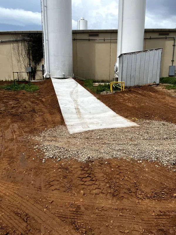 Concrete ramp between two white industrial tanks, leading from the ground up to the tanks, set outdoors.
