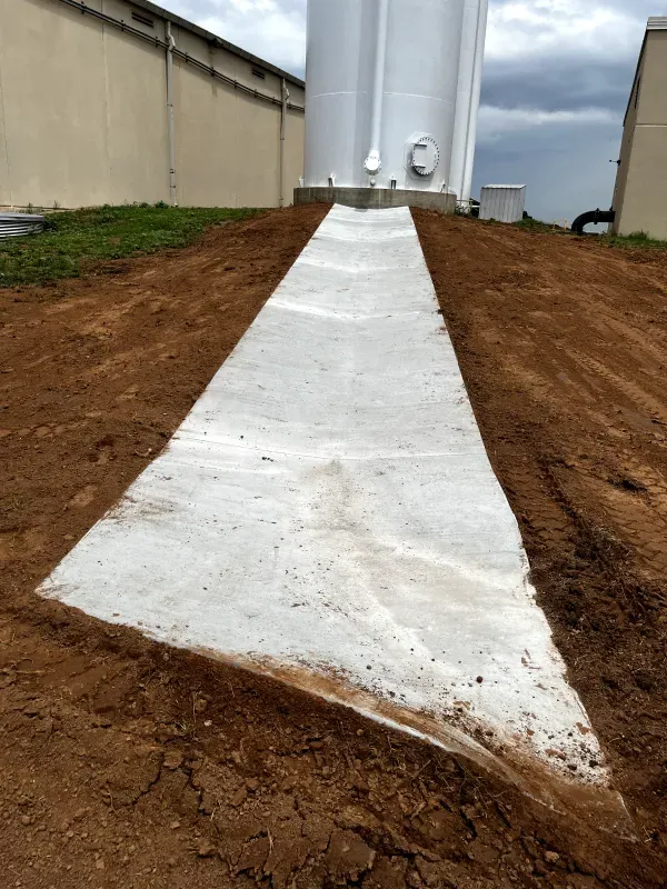 Concrete pathway leading up to a large white tank, surrounded by dirt and grass.