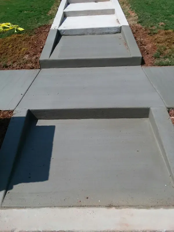 Concrete walkway with inset features and steps leading to grass.