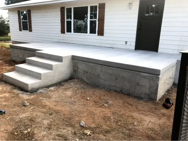 Concrete porch with steps leading to the front door of a white house with brown shutters.