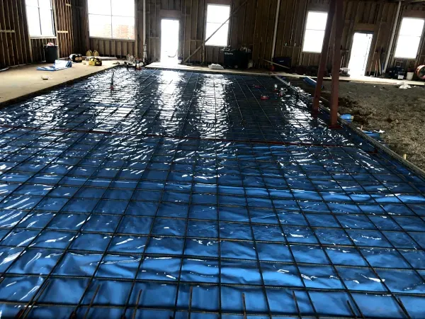 Interior construction site with rebar grid laid on blue plastic, ready for concrete pouring.