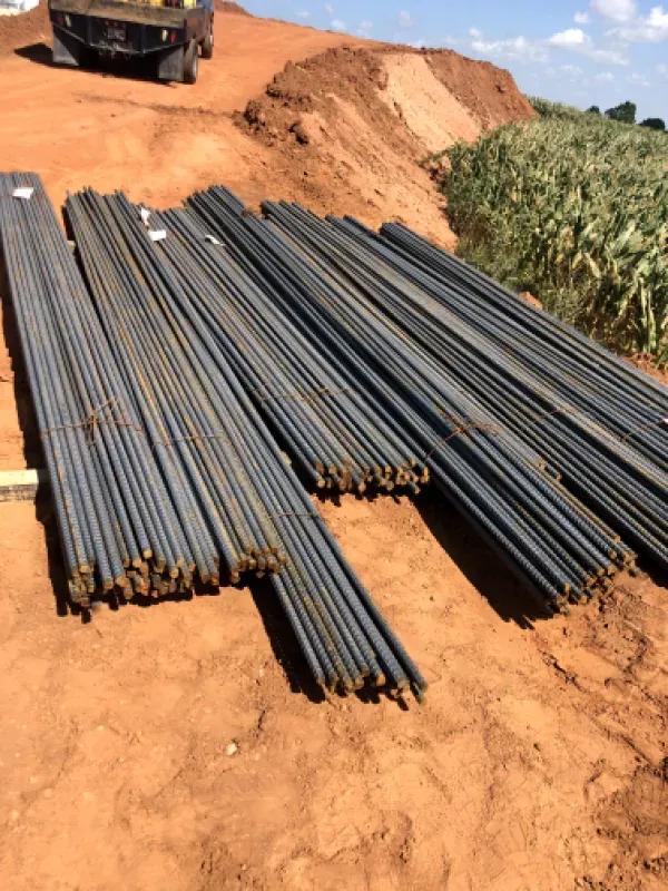 Piles of rebar rods on red dirt, construction site, with a truck and dirt mound in the background.