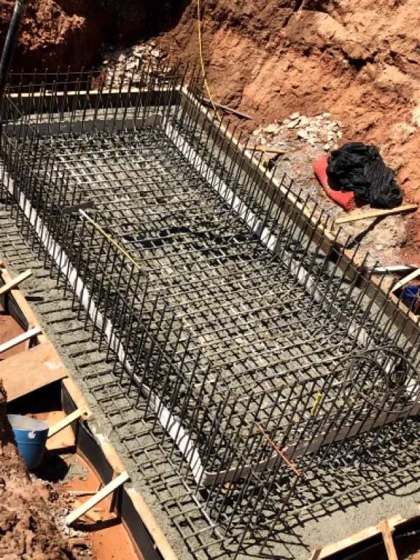 Construction site: rectangular concrete form with steel rebar framework; dirt surrounds.