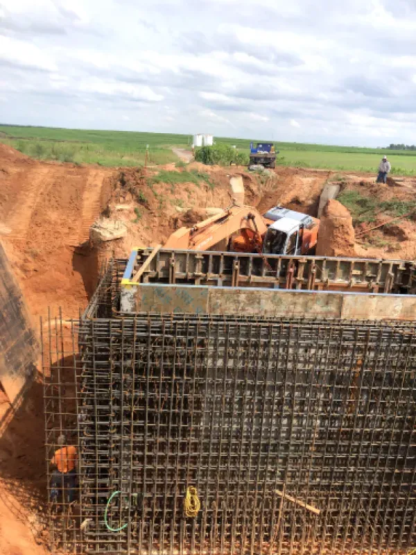 Construction site with concrete forms, rebar cage, and heavy machinery, set in a rural area.