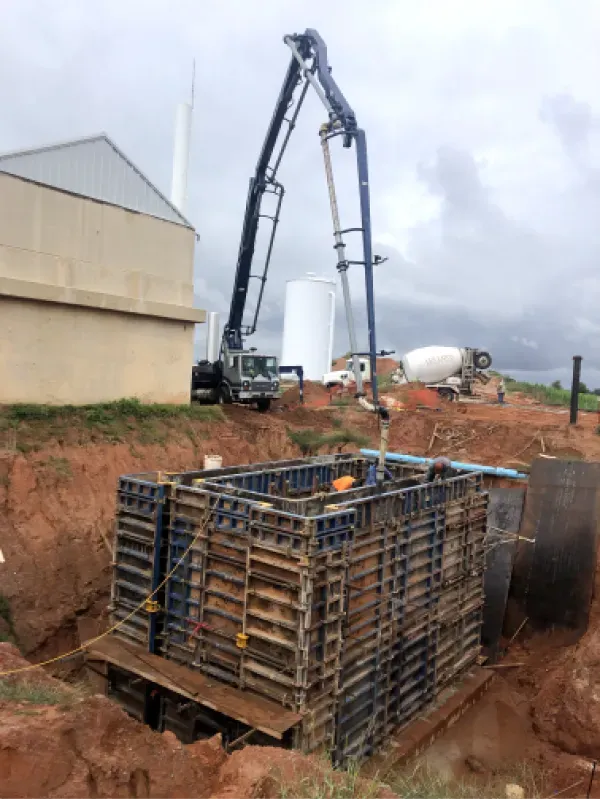 Concrete pump truck pouring concrete into a formwork structure in an excavated pit.