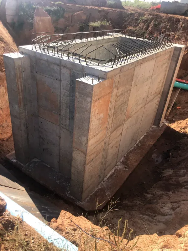Concrete structure, rectangular, with rebar framework at top, in a construction site.