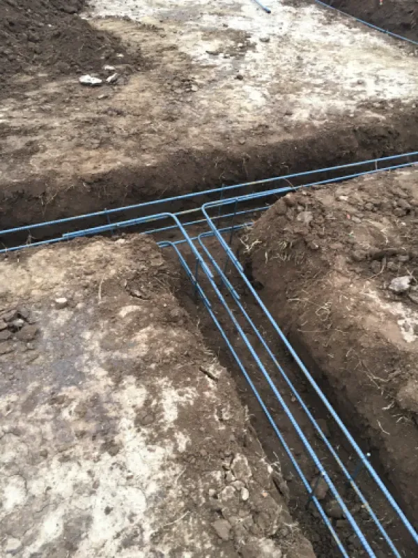 Blue pipes laid in trenches, likely for underground utility installation, in a dirt construction site.