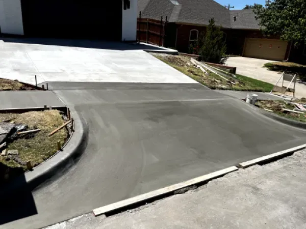 Freshly poured concrete driveway and sidewalk, curved design, adjacent to a house with a garage and lawn.