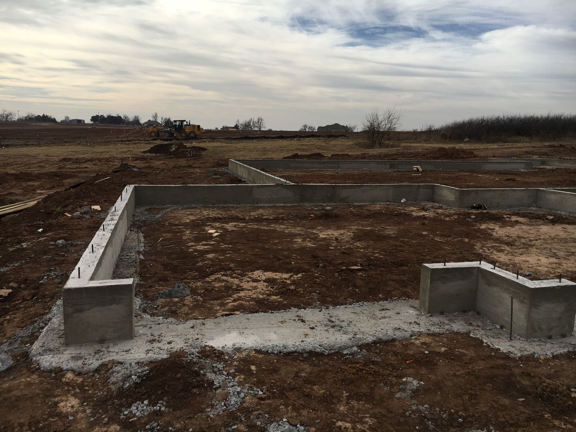 Concrete foundation of a building under construction on a dirt lot, cloudy sky in background.
