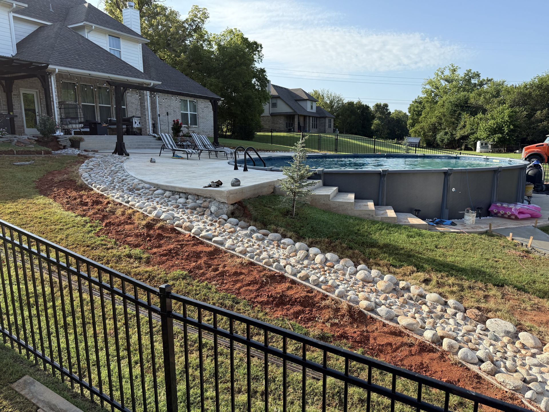 Backyard with pool, black fence, rock landscaping, and house.