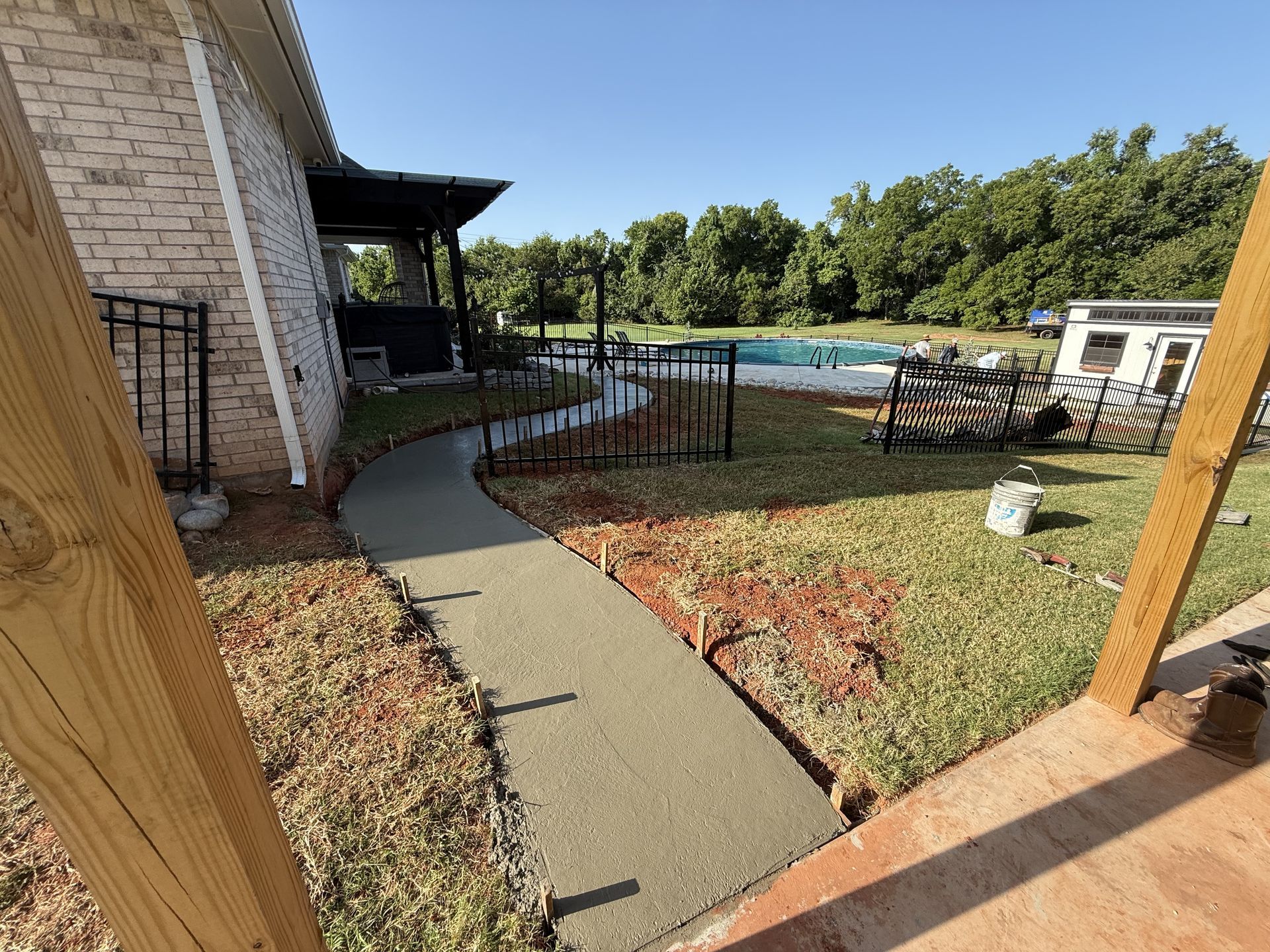 New concrete pathway next to a brick house and leading toward a pool in a grassy yard.