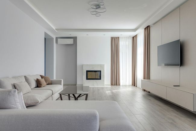 Modern living room with a gray sectional, fireplace, wall-mounted television, and beige curtains.