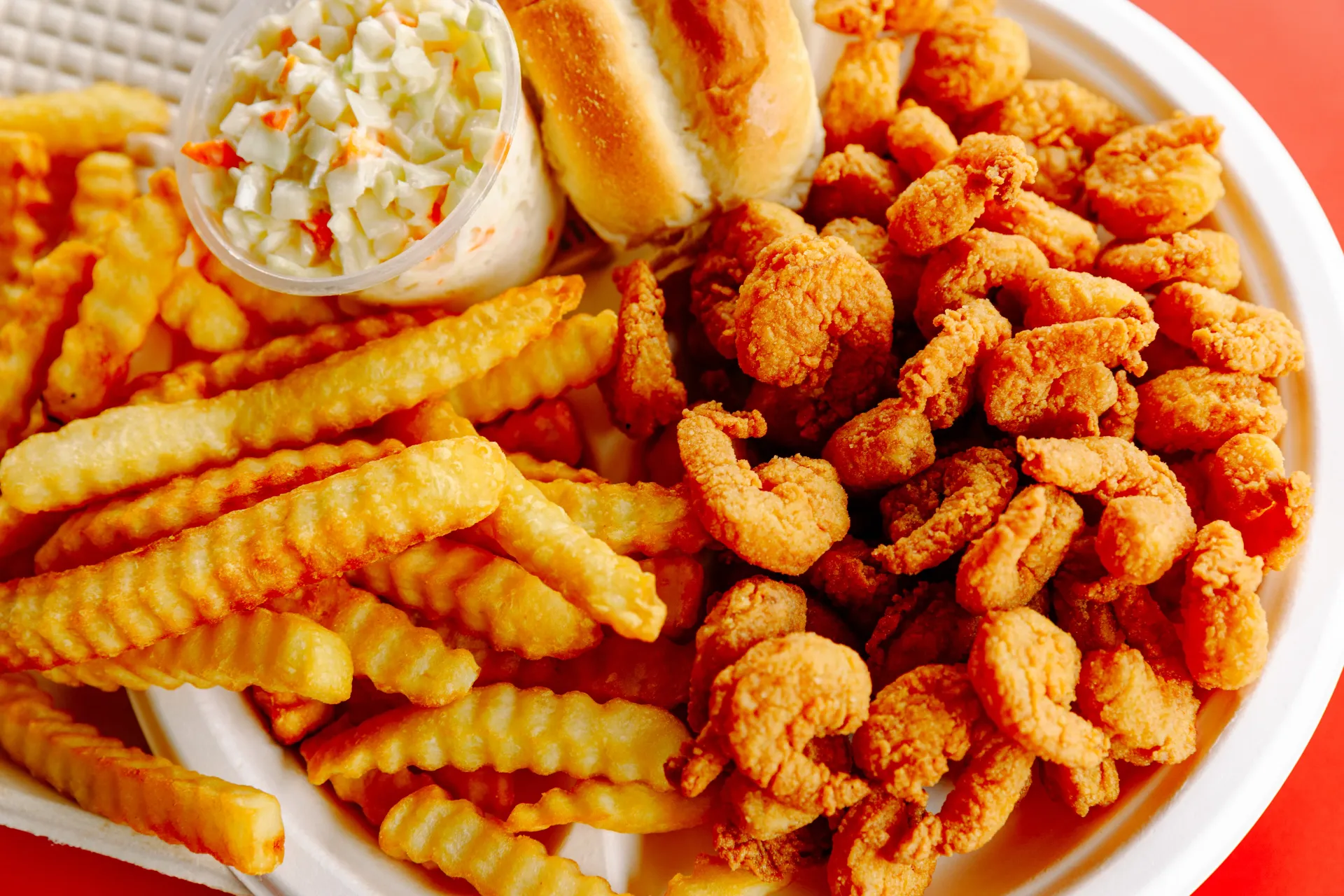 Plate of fried chicken tenders, crinkle-cut fries, coleslaw, and bread roll on a white plate.
