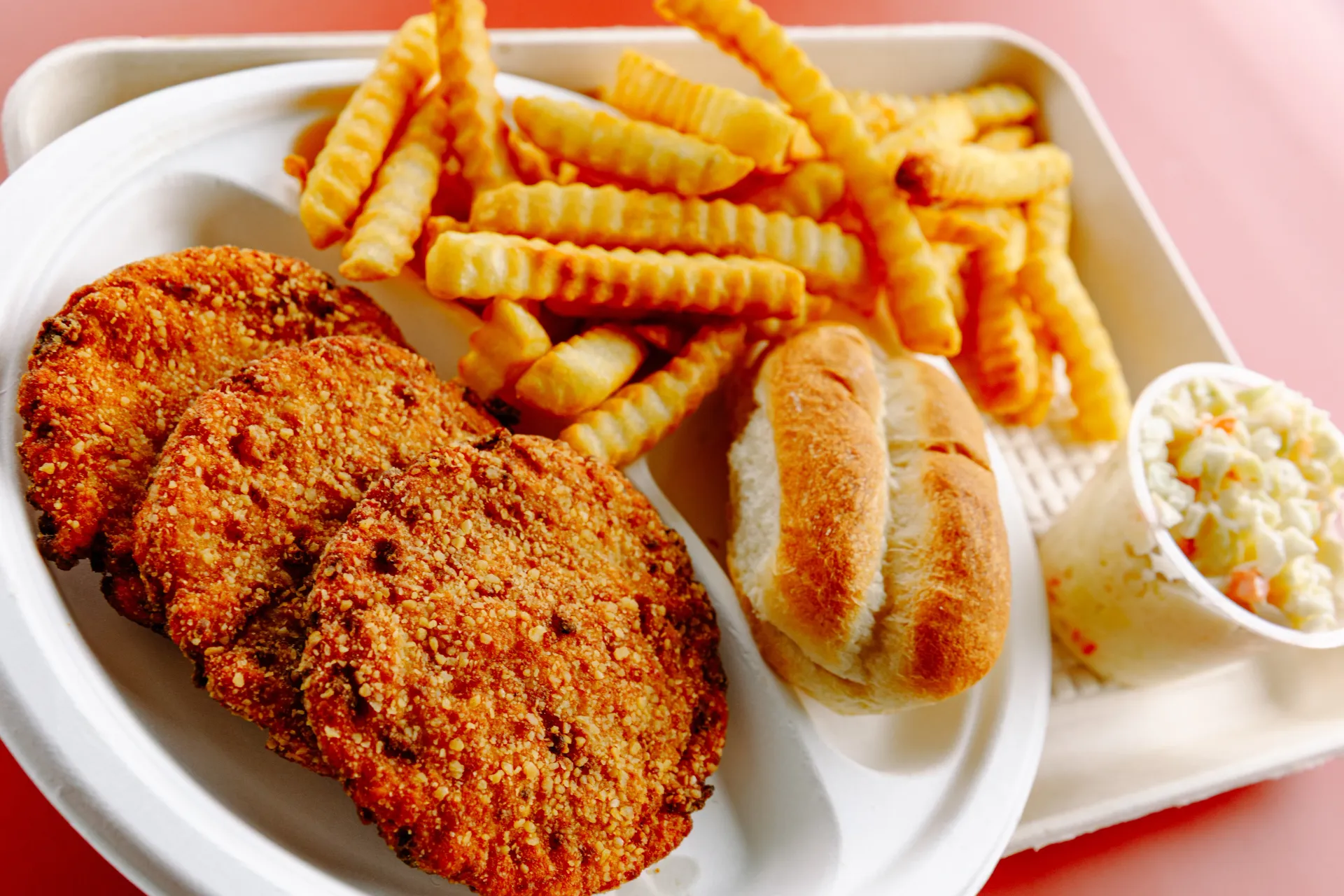 Breaded cutlets with crinkle-cut fries, roll, and coleslaw on a white plate