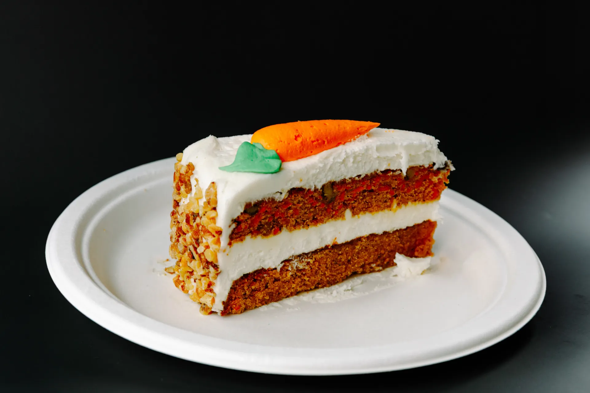 Slice of carrot cake with white frosting and orange garnish on a white plate
