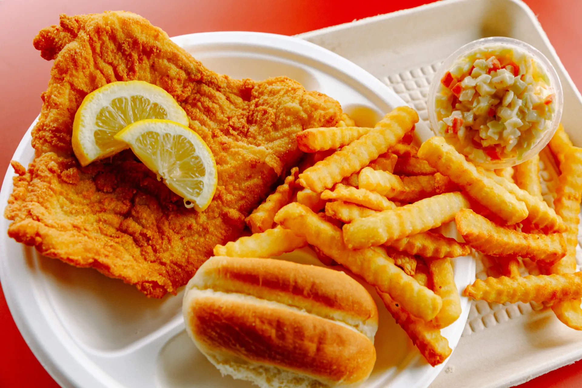 Fried chicken, crinkle-cut fries, a sandwich, coleslaw, and lemon wedges on a takeout tray