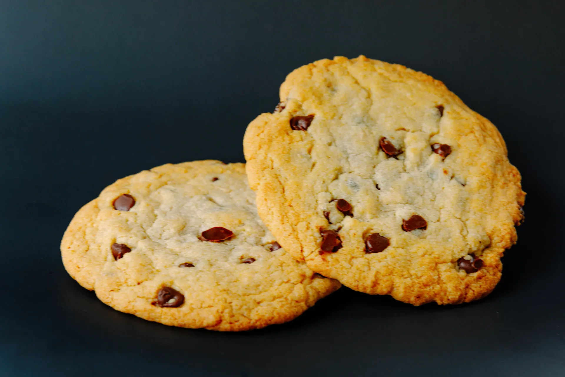Two chocolate chip cookies on a dark background