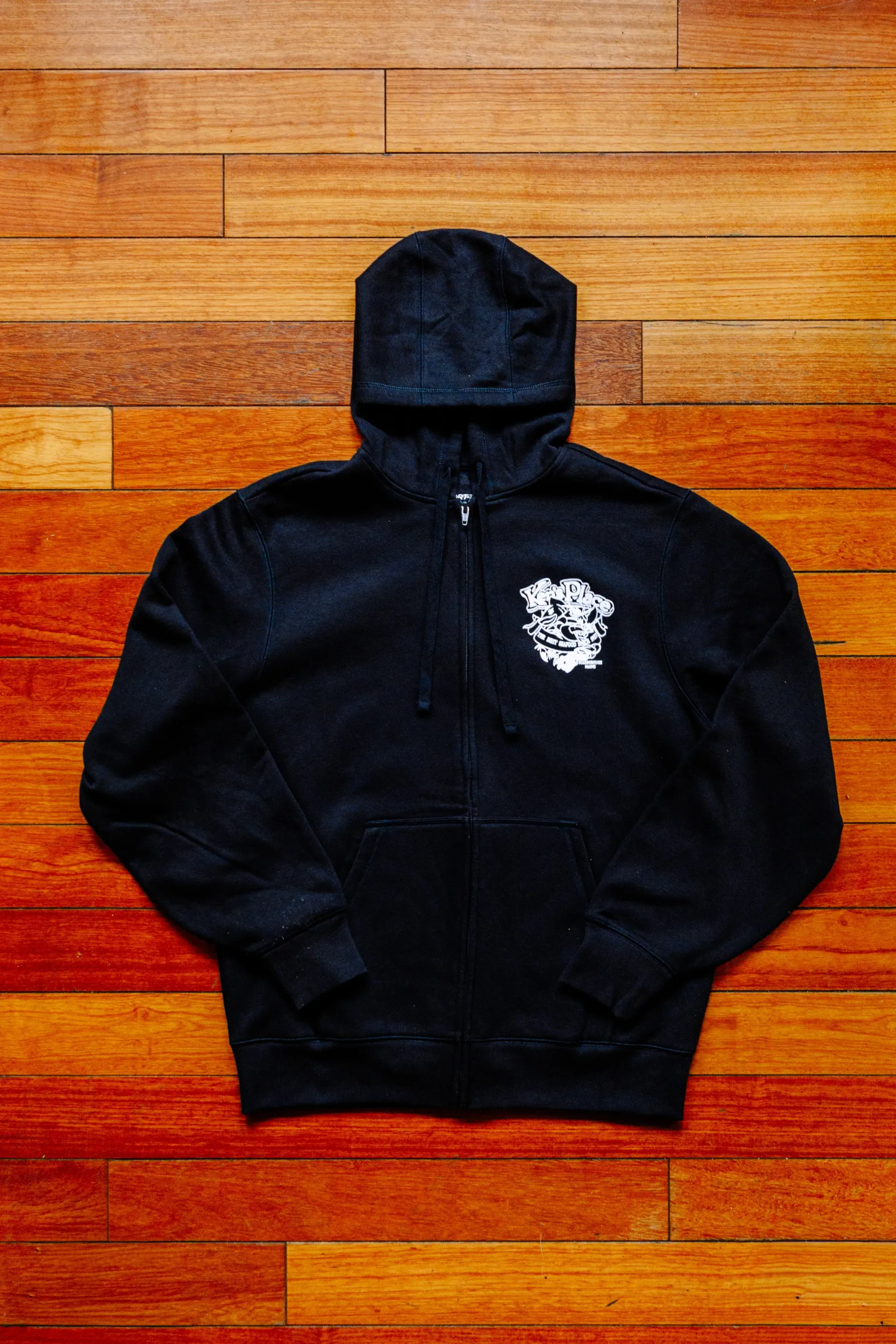 Red hoodie with colorful graphic logo laid flat on a wooden floor.