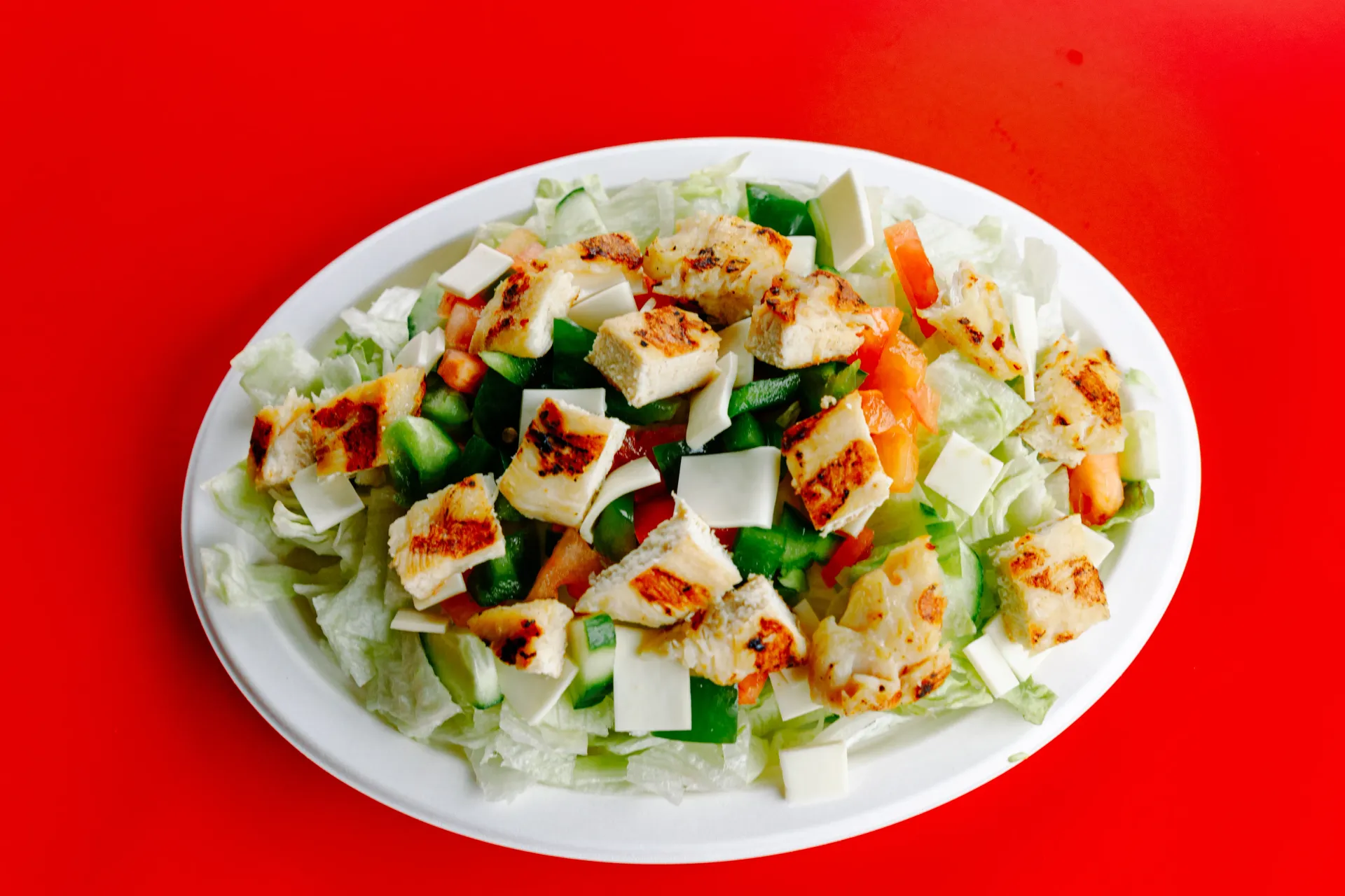 A plate of salad with cucumber, tomato, lettuce, and seasoning on a bright red background