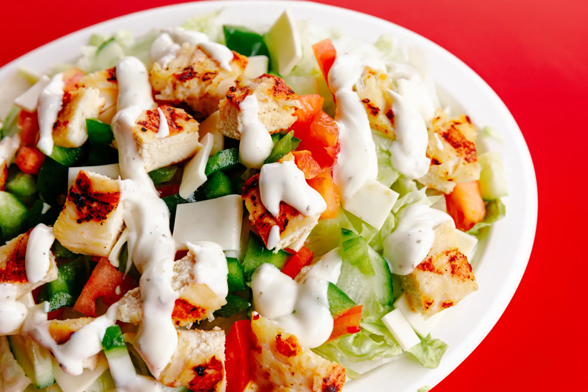 Close-up of a salad with cucumbers, tomatoes, lettuce, croutons, and creamy dressing in a white bowl