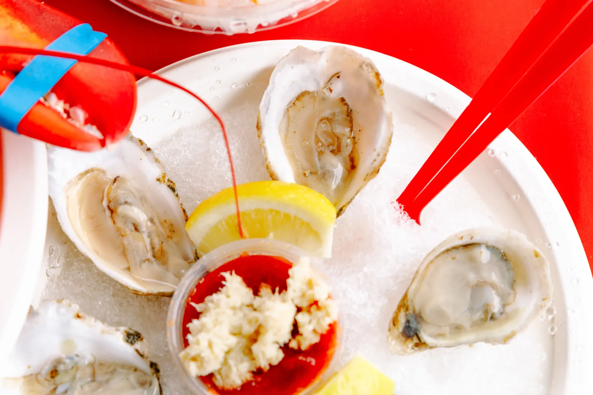 Oysters on ice with lemon wedges, red utensils, and a small cup of sauce on a white plate