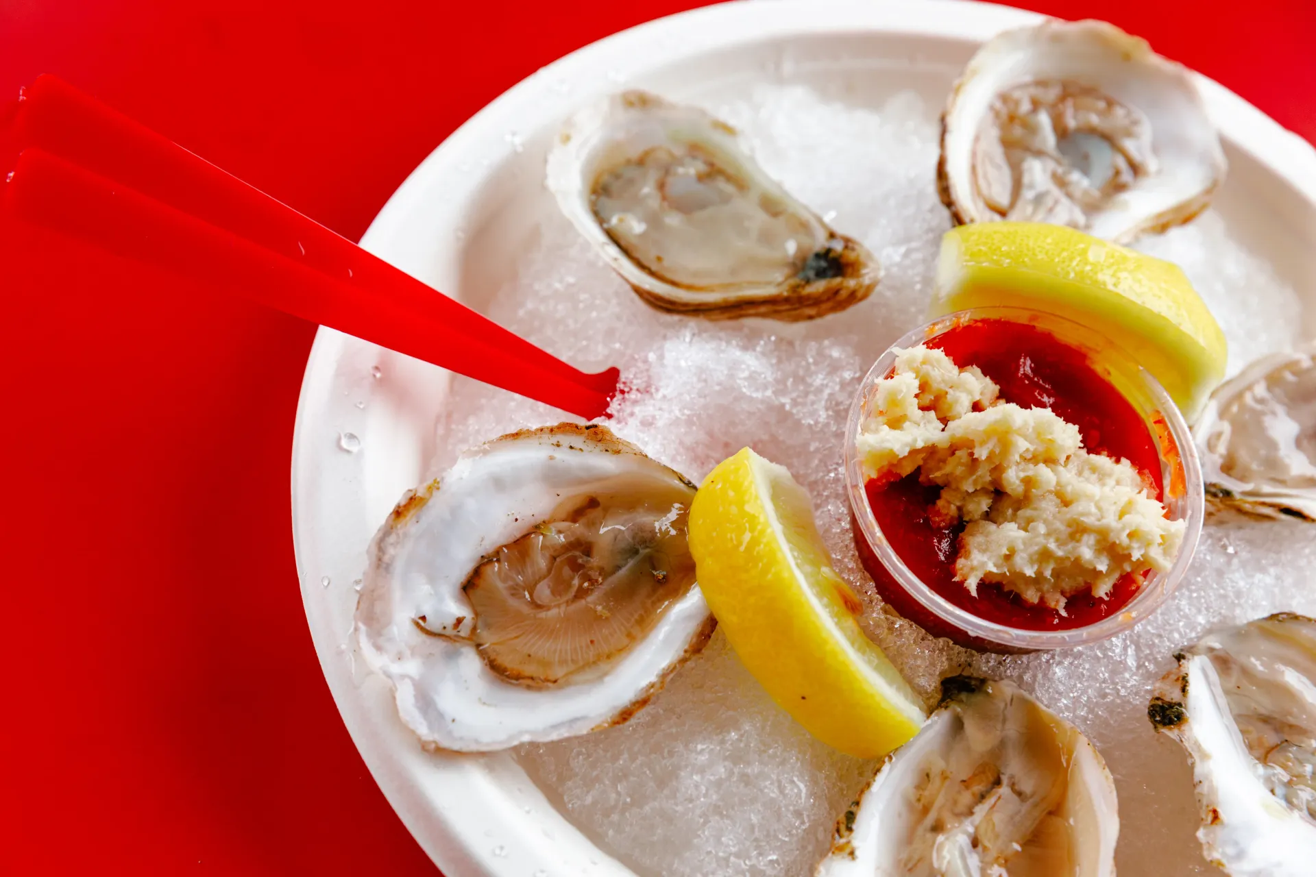 Oysters on ice with lemon wedges and cocktail sauce, with a red straw pointing at one oyster