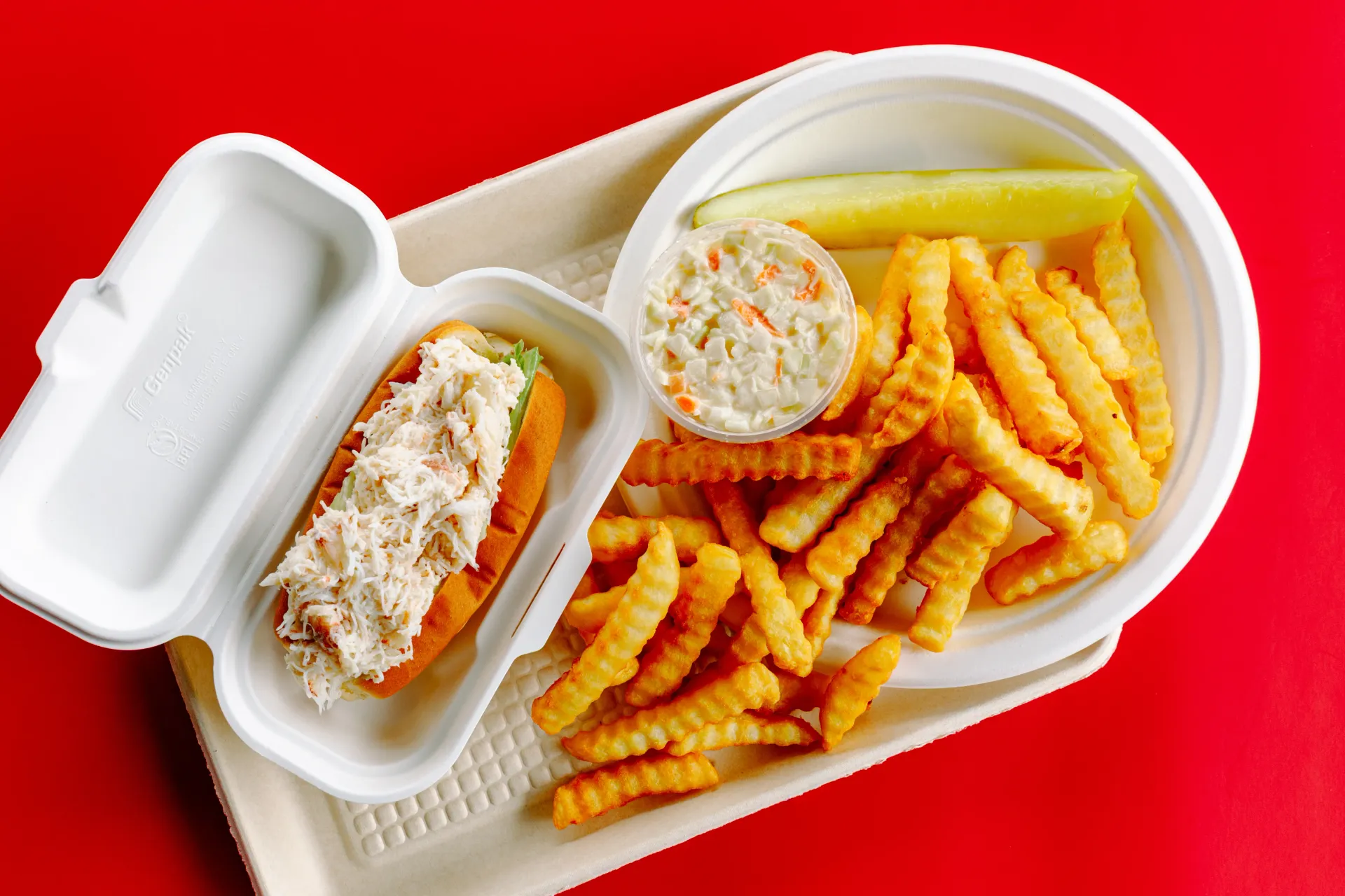 Takeout container with fries and two dipping sauces on a red background