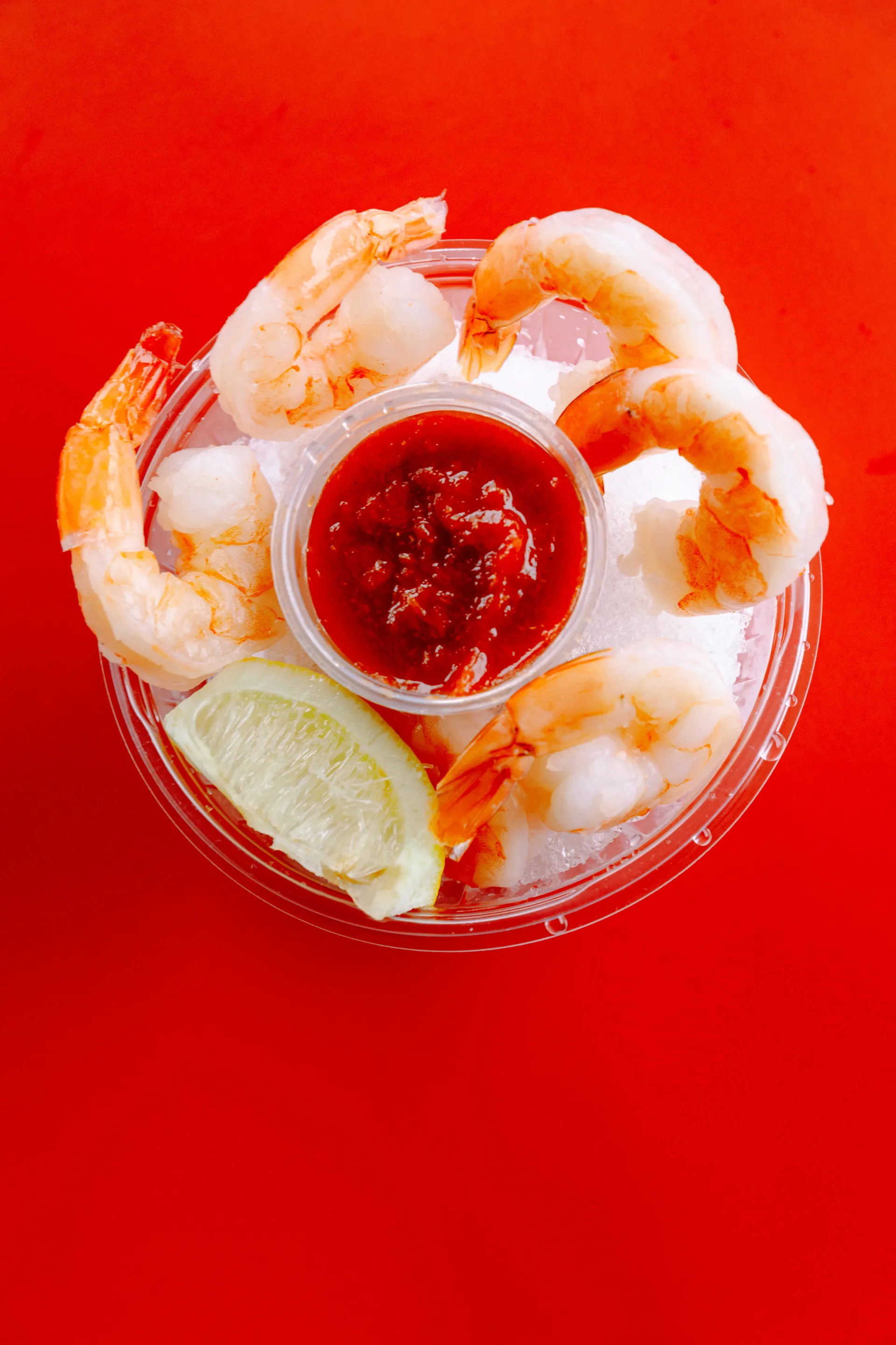 Shrimp cocktail with lemon wedge and red dipping sauce on a bright red background
