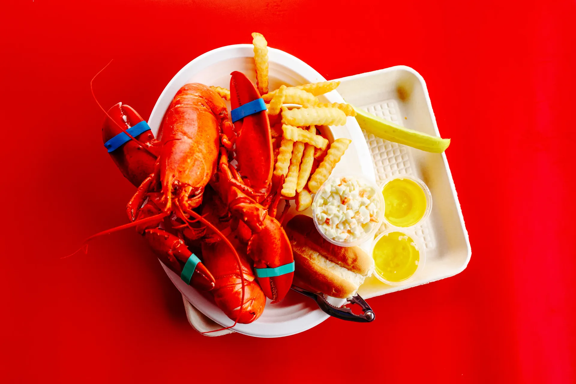 Red seafood platter with lobster, fries, corn, and lemon wedges on a white tray