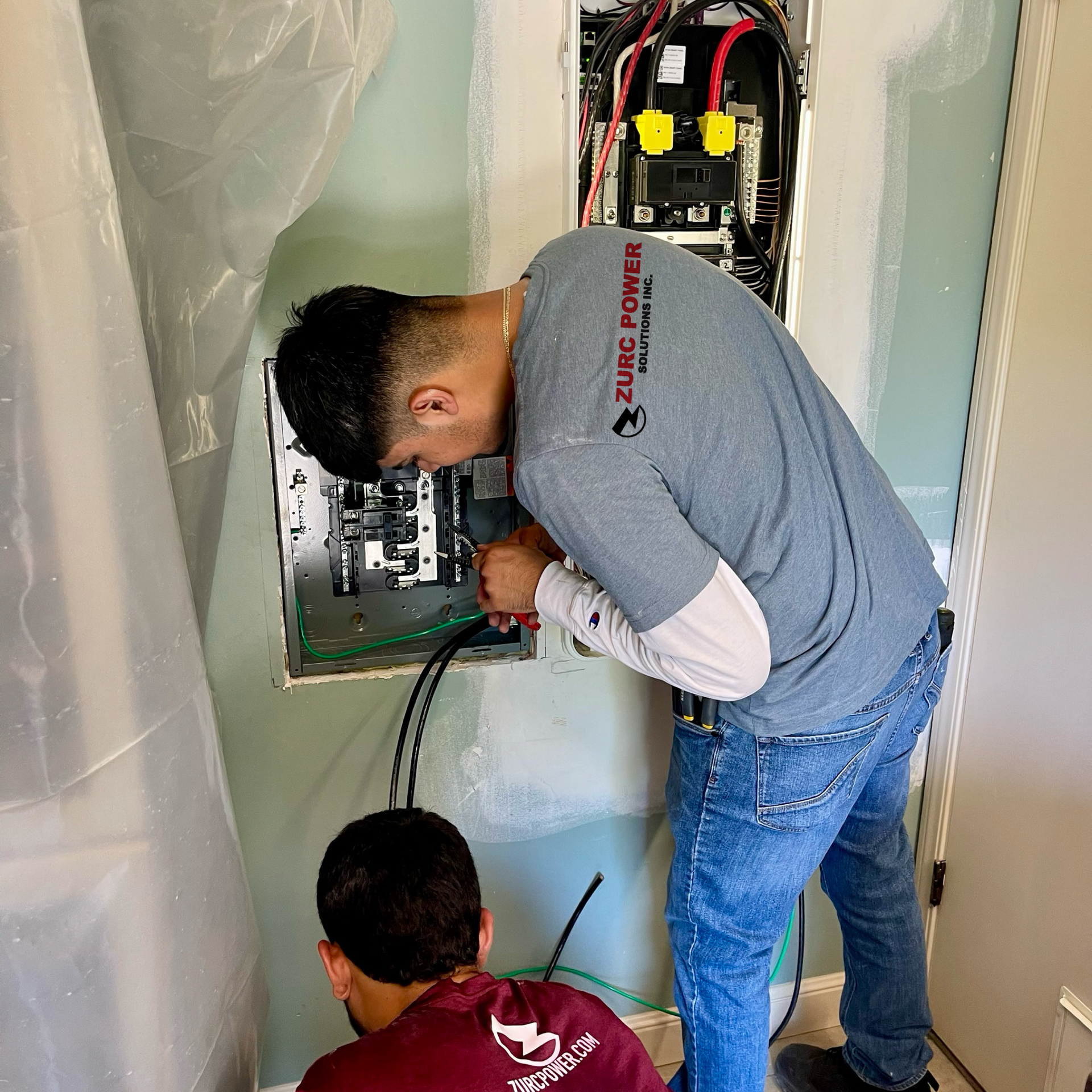 Two men are working on an electrical box in a room.