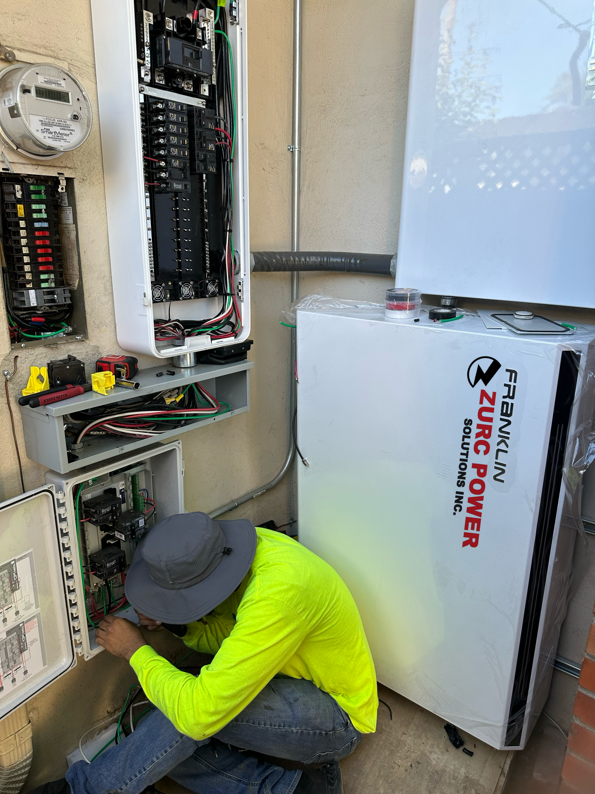 A man in a yellow shirt is working on an electrical box.