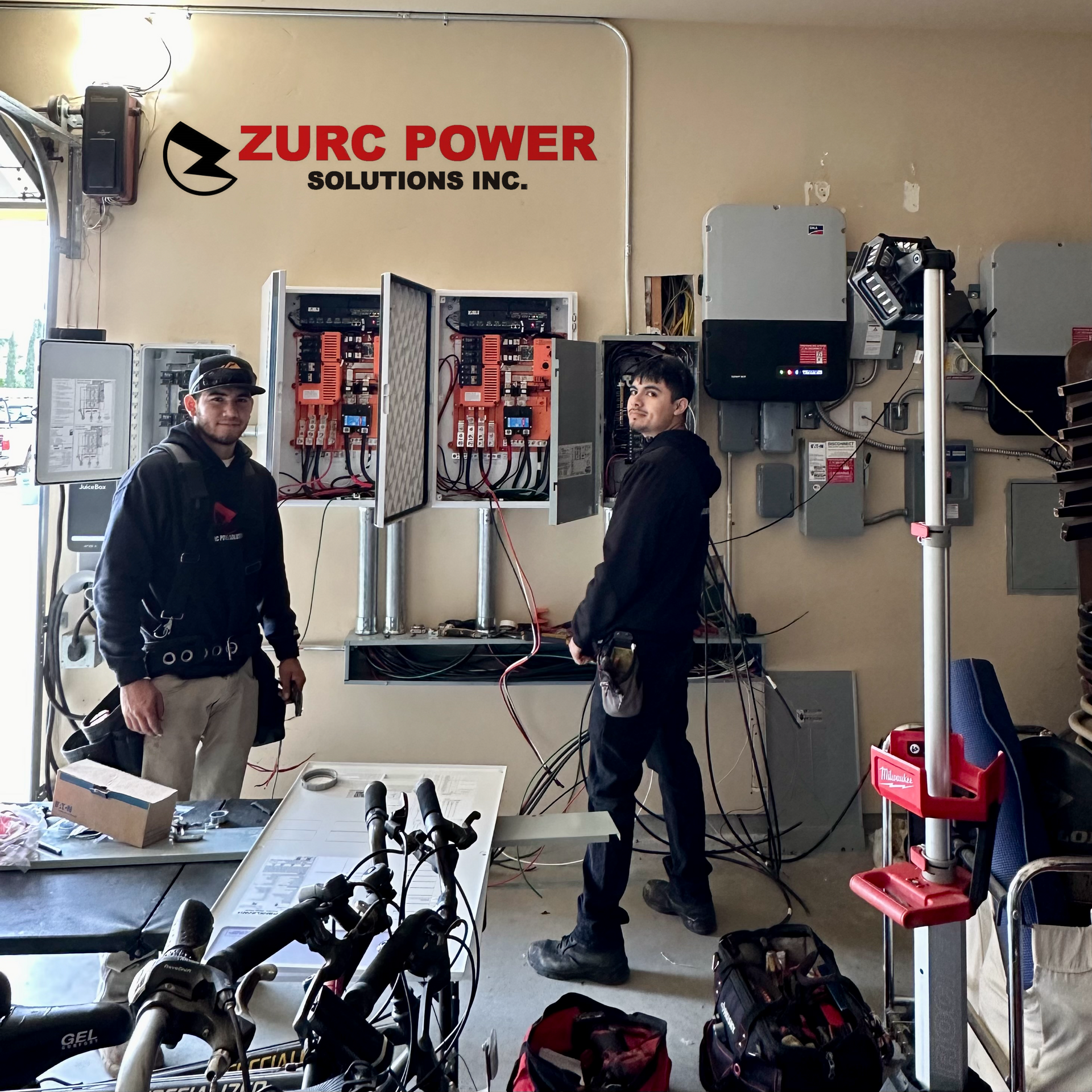 Two men standing in front of a wall that says zurc power solutions inc.