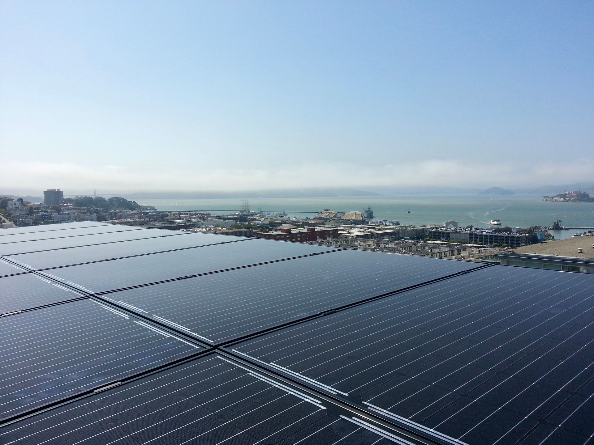 A row of solar panels on top of a building with a city in the background