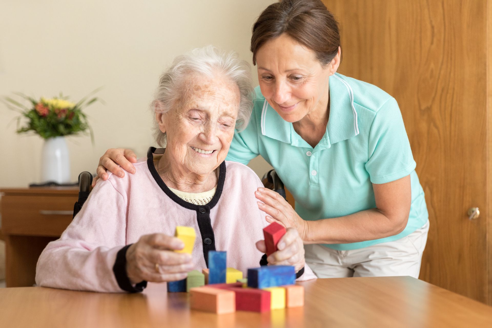 an elderly woman is playing with wooden blocks with a nurse .