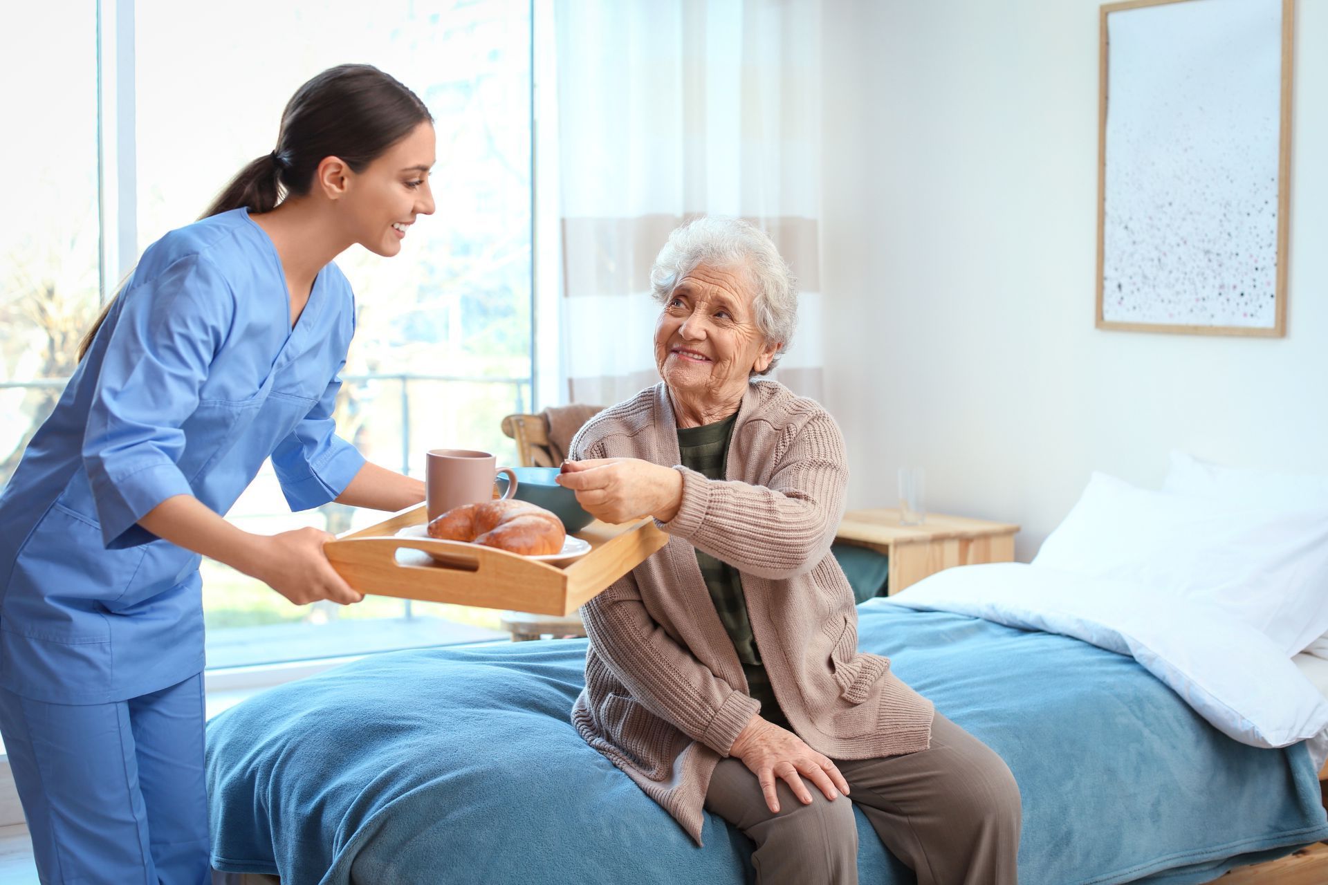 a nurse is serving a cup of coffee to an elderly woman sitting on a bed .