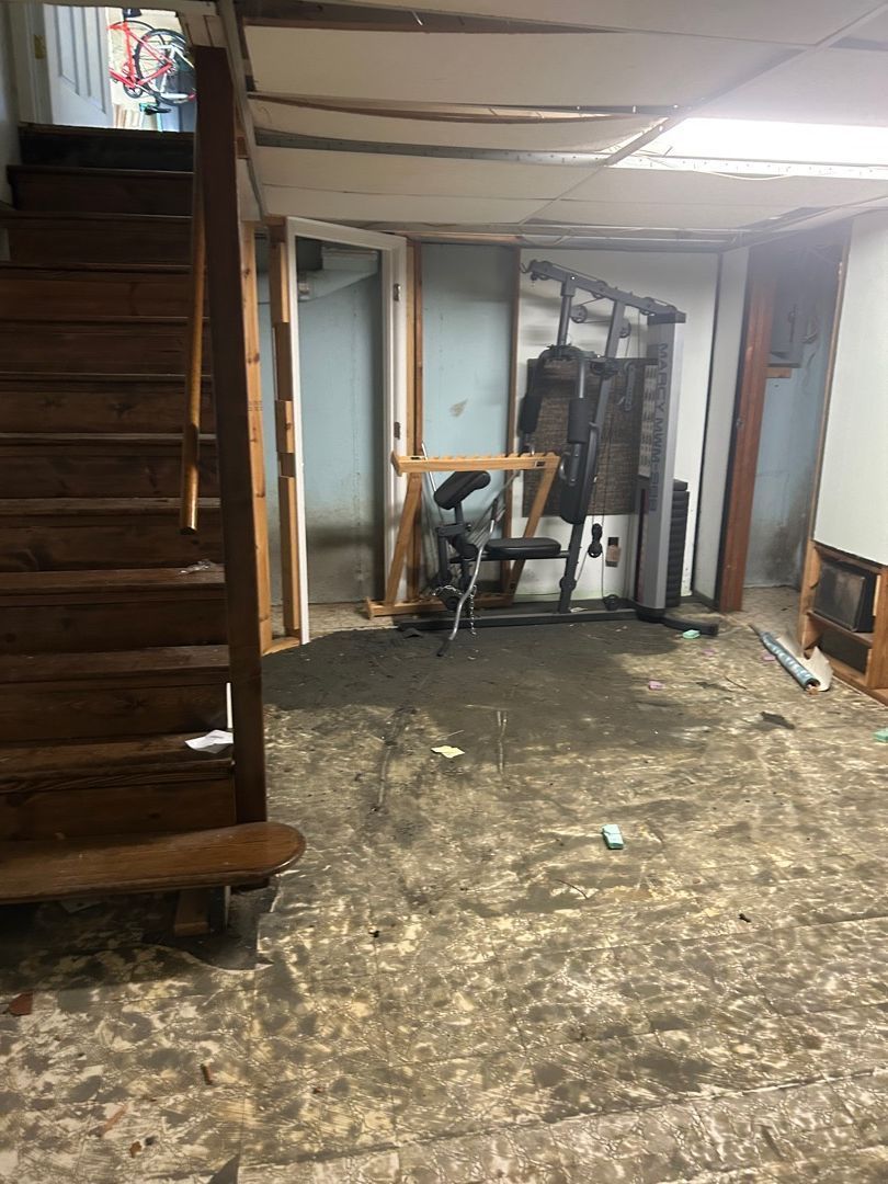 Basement bedroom area after pack-out and drywall removal, showing exposed studs and concrete