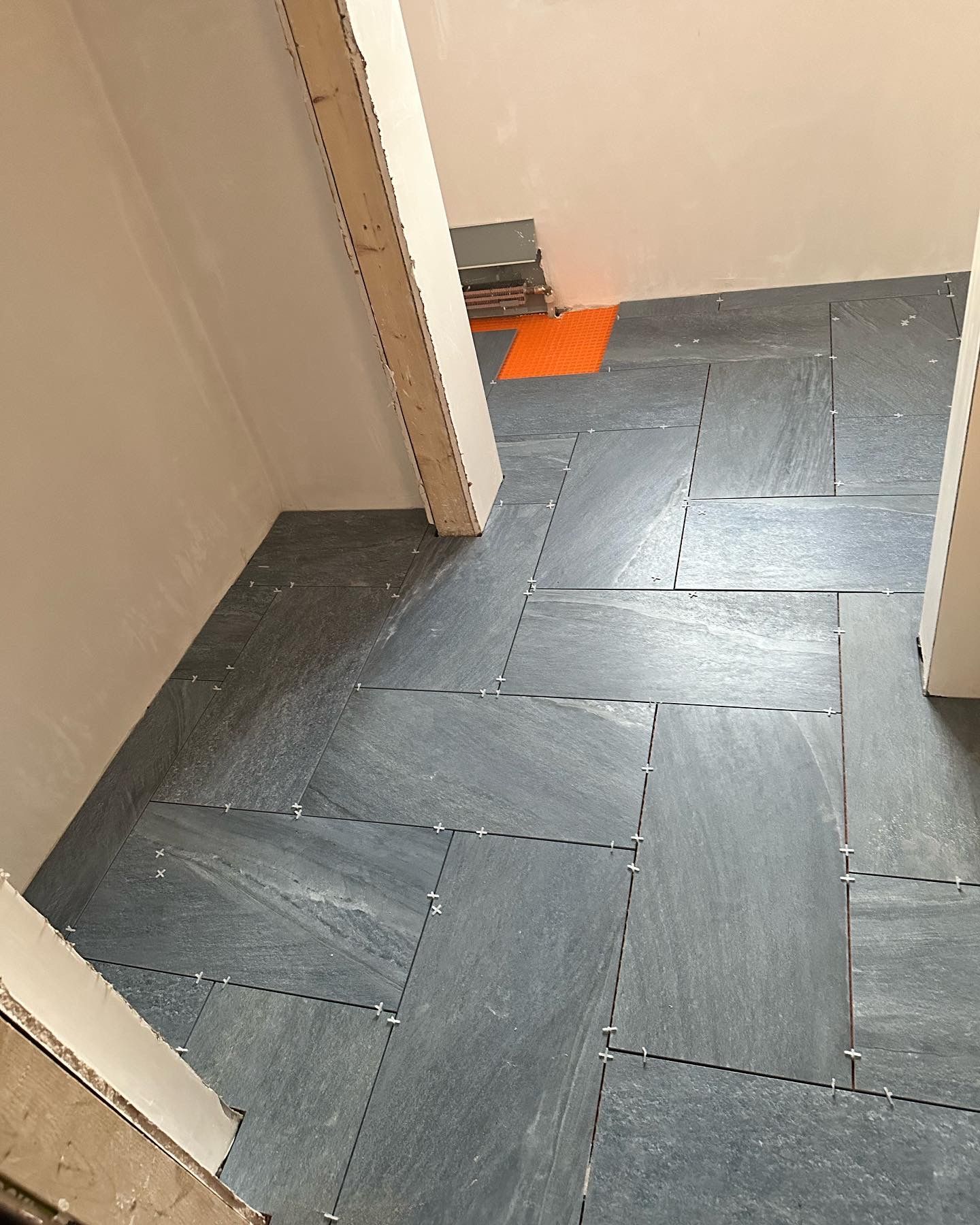 Dark gray slate tiles being installed in a doorway. Orange floor patch visible.