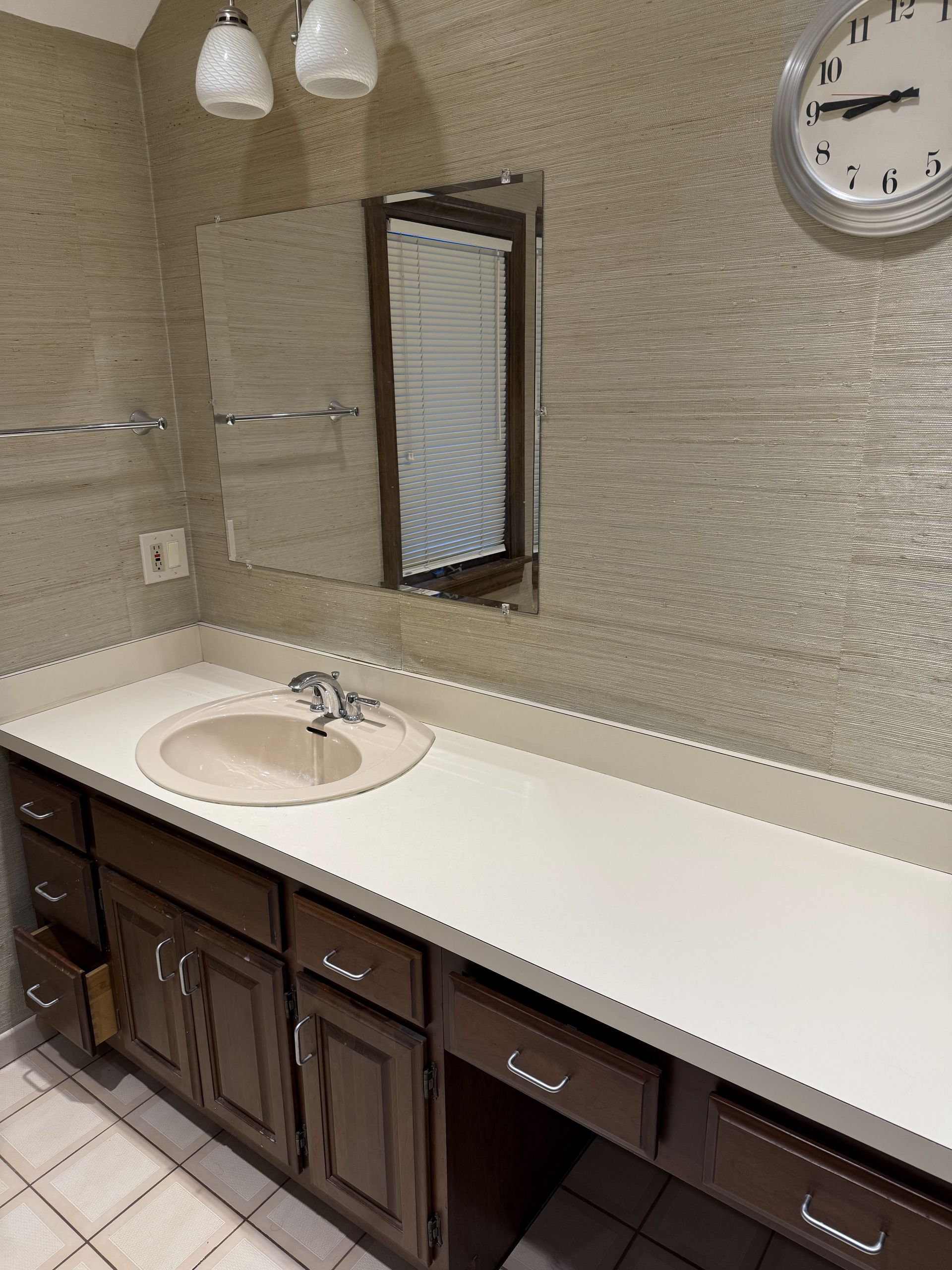 Bathroom with beige textured wall, dark brown cabinets, a white countertop, and a round sink.
