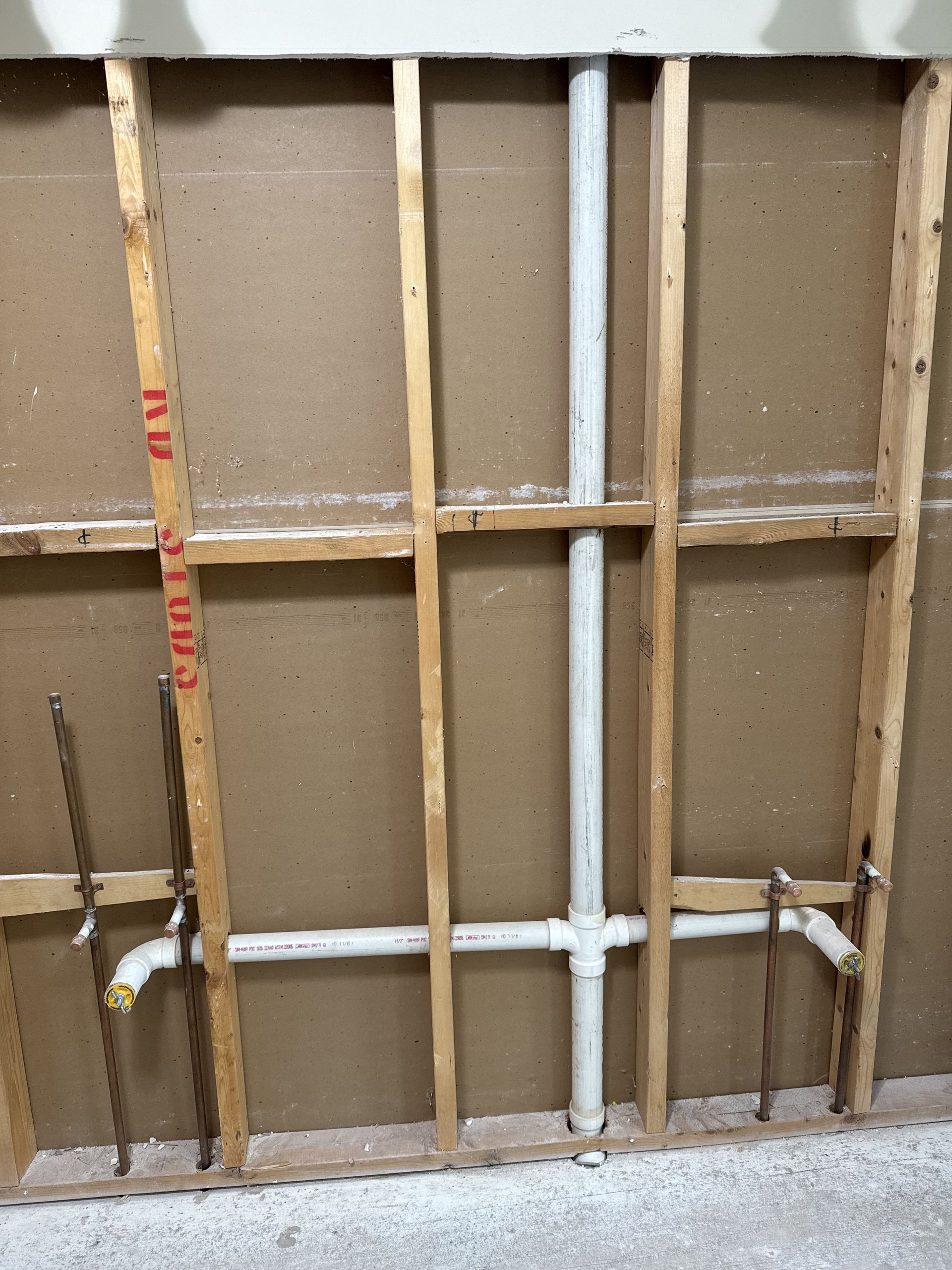 Framing and plumbing pipes inside a wall cavity, with horizontal and vertical white pipes.