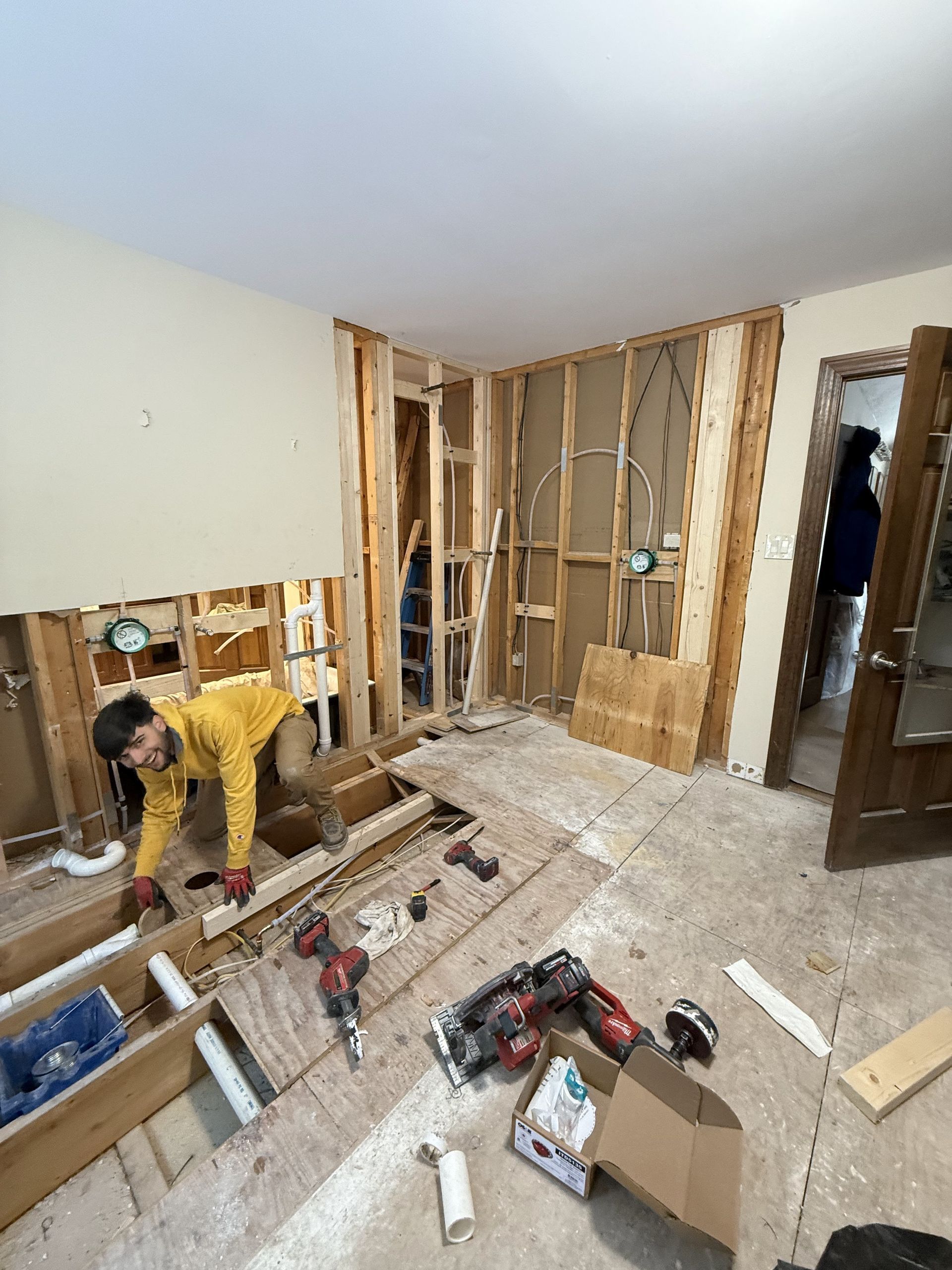 Man working on bathroom renovation, wooden framing exposed. Power tools and debris on the floor.