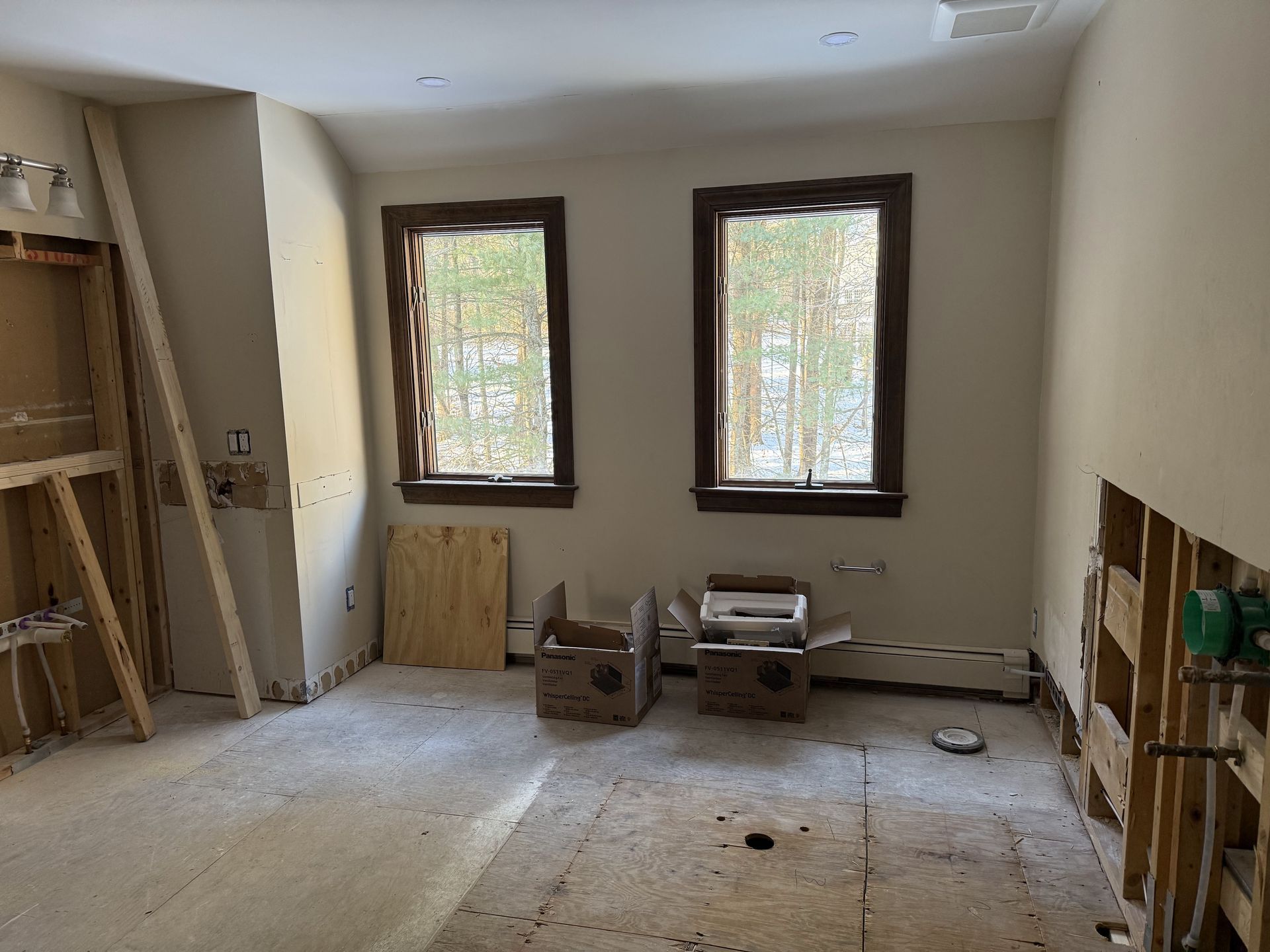 Bathroom under construction with exposed framing, two windows, and debris on the floor.
