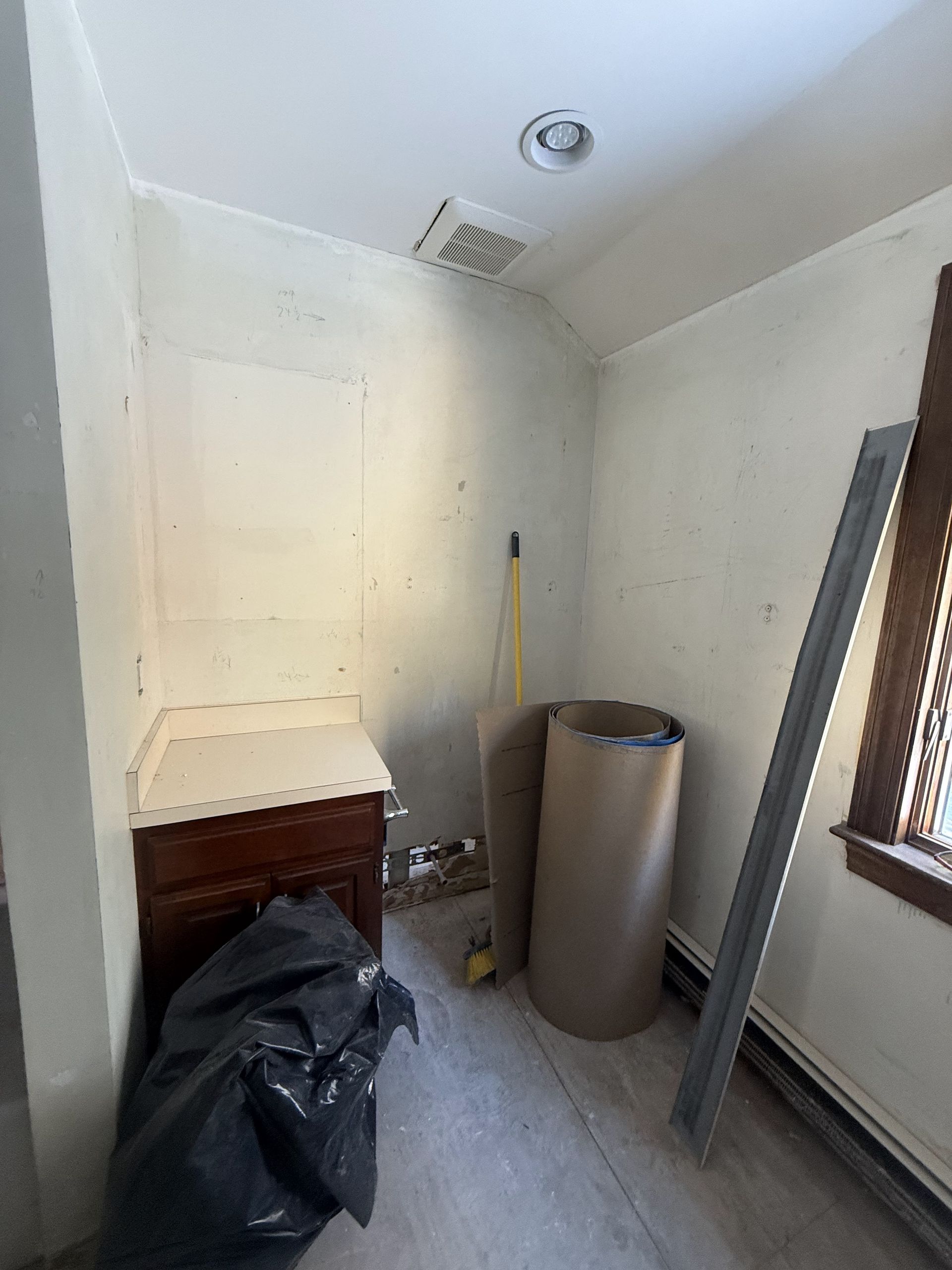 Small room under construction, with dark wood cabinet, trash bag, and cardboard roll.