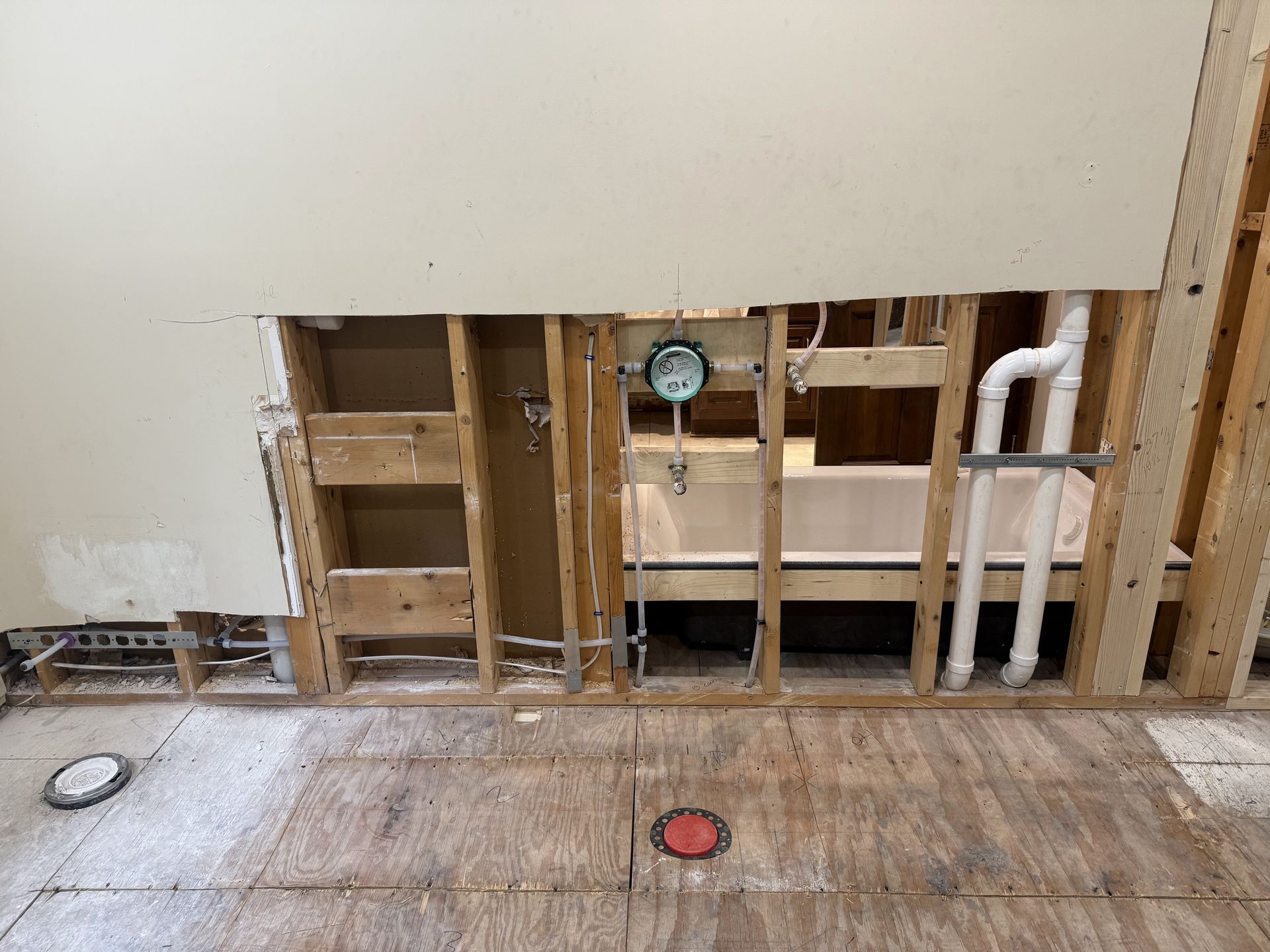 Bathroom wall under construction, showing framing, plumbing, and a partially visible bathtub.