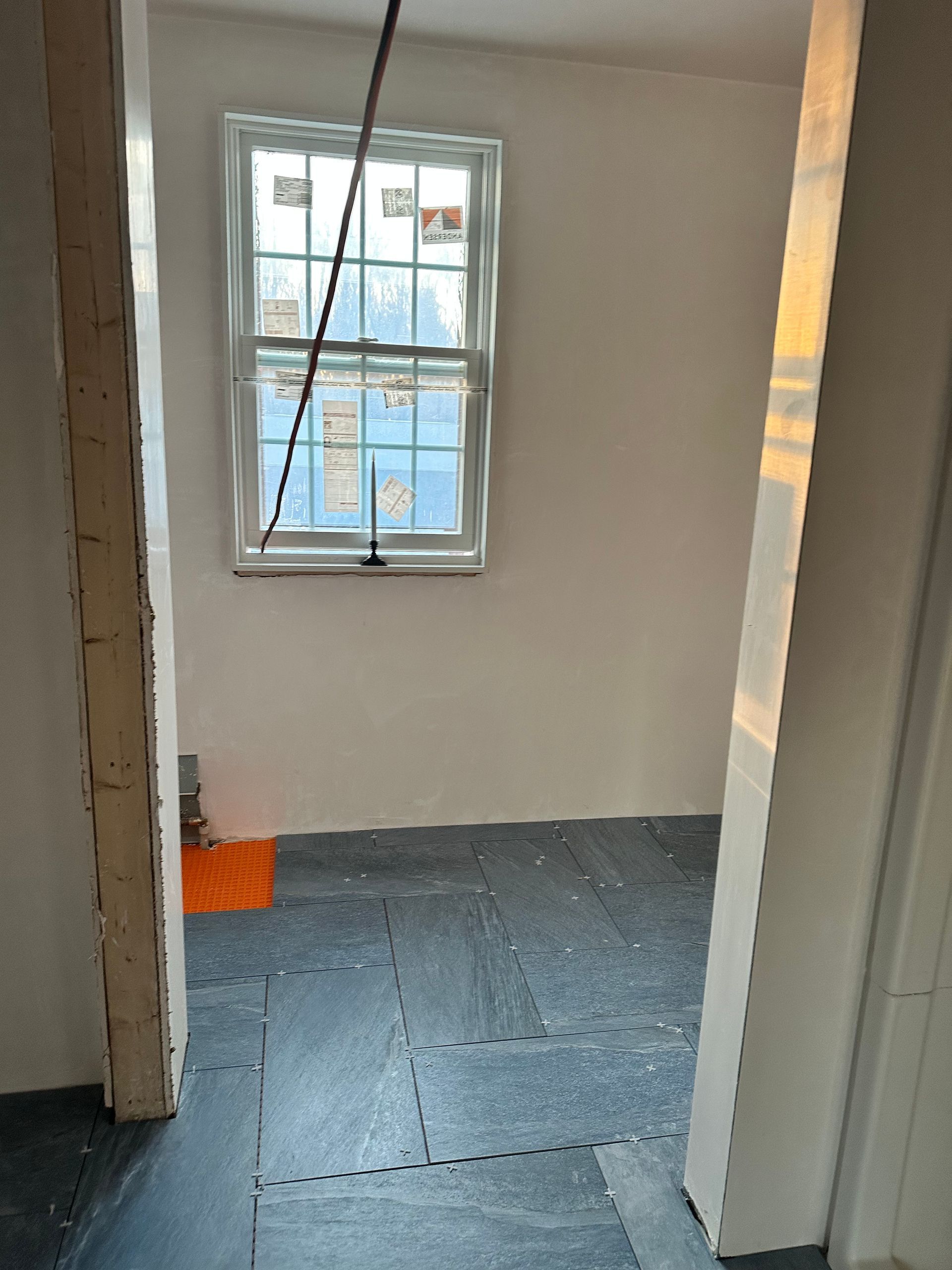Interior view of a room with a window, white walls, and dark gray flooring. Partially constructed doorway visible.